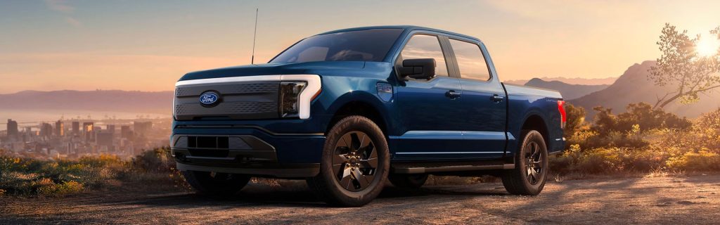 2025 Ford F-150 Lightning electric pickup truck parked overlooking the Saint Louis skyline at sunset, showcasing its bold front grille and modern design